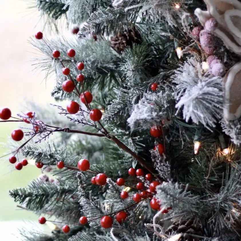 Frosted Christmas tree branches decorated with red berries, pinecones, and warm white lights.