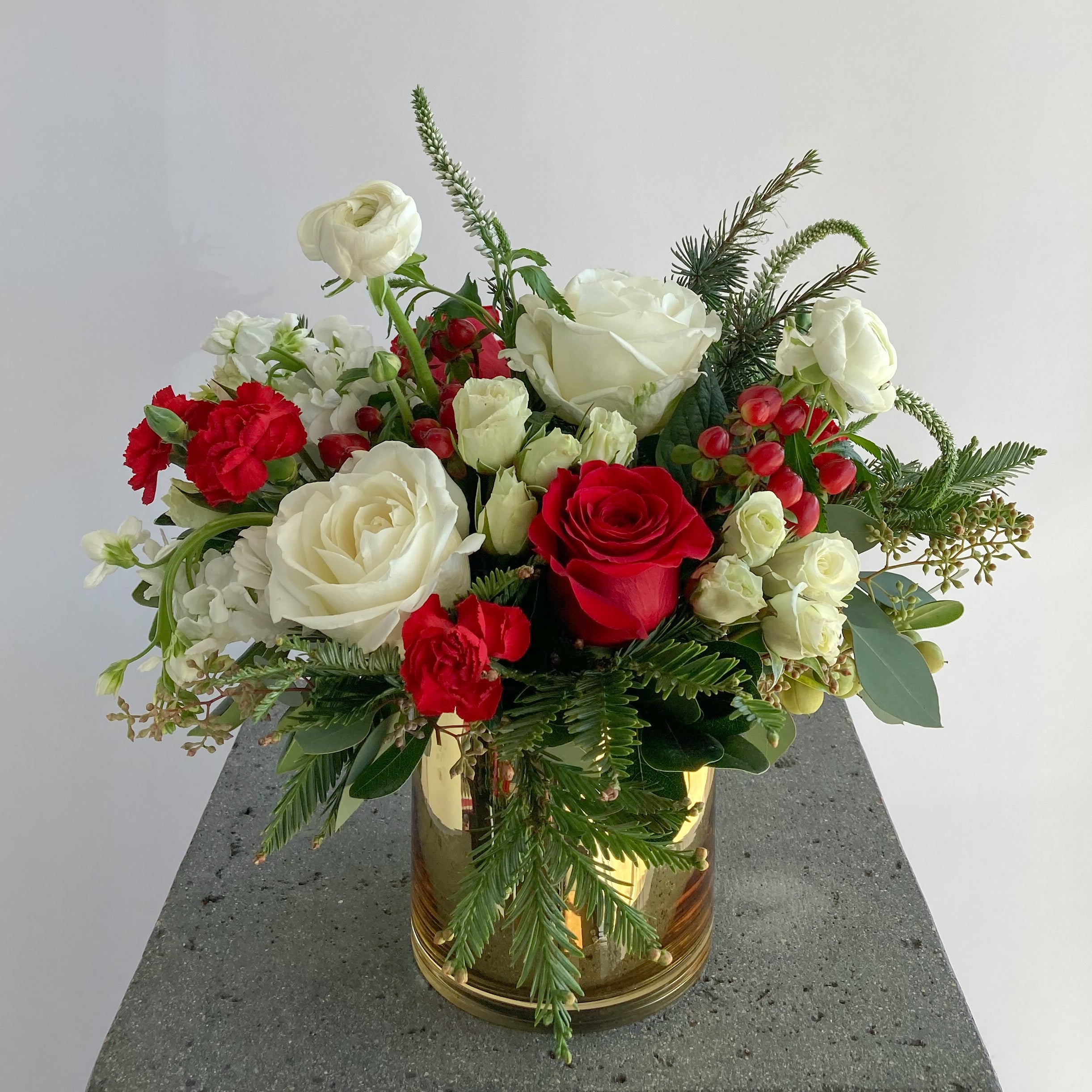 Bouquet of red and white flowers with seasonal greenery in a gold vase 
