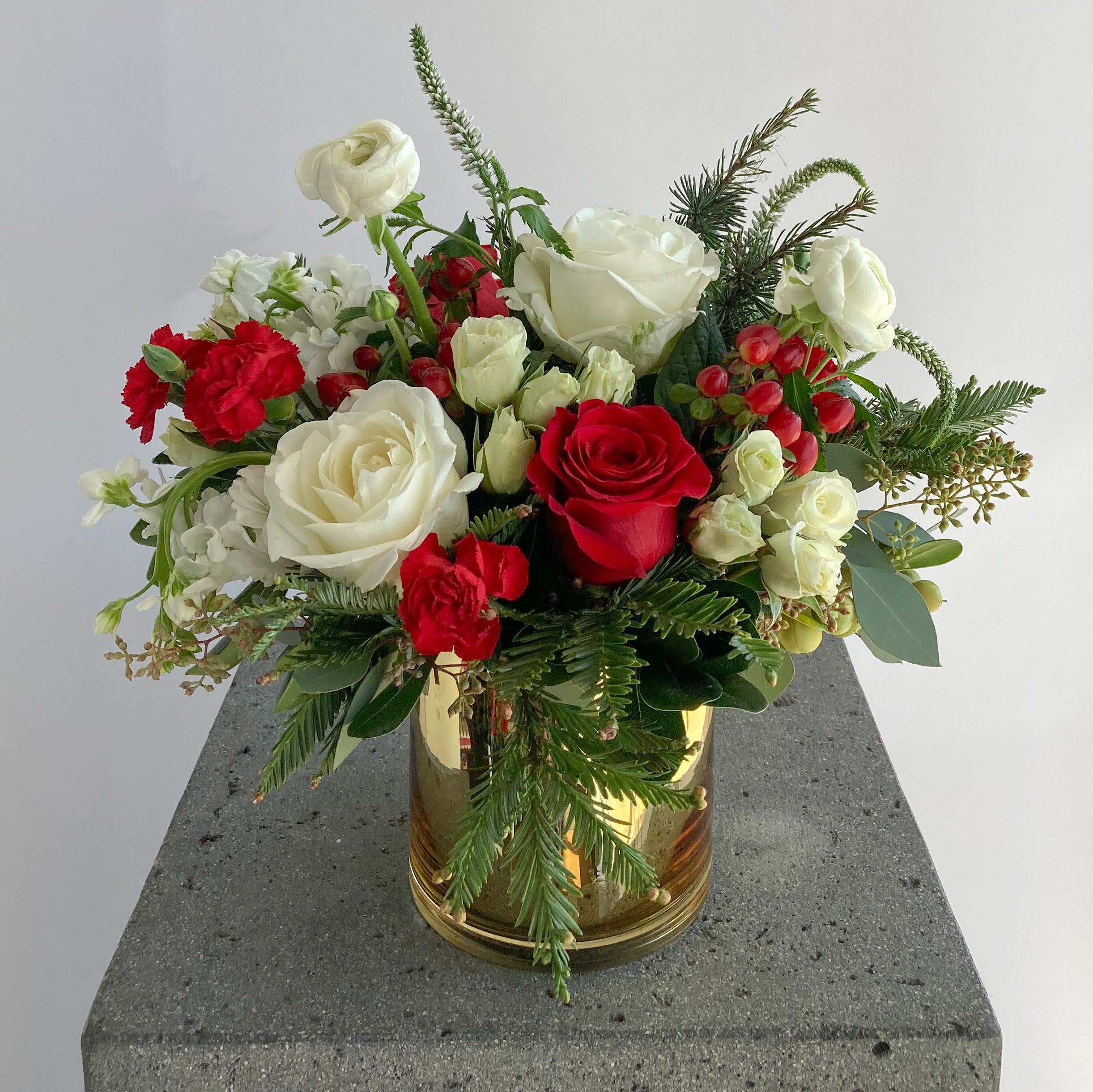 Red and white Christmas flower arrangement with greenery in a gold vase