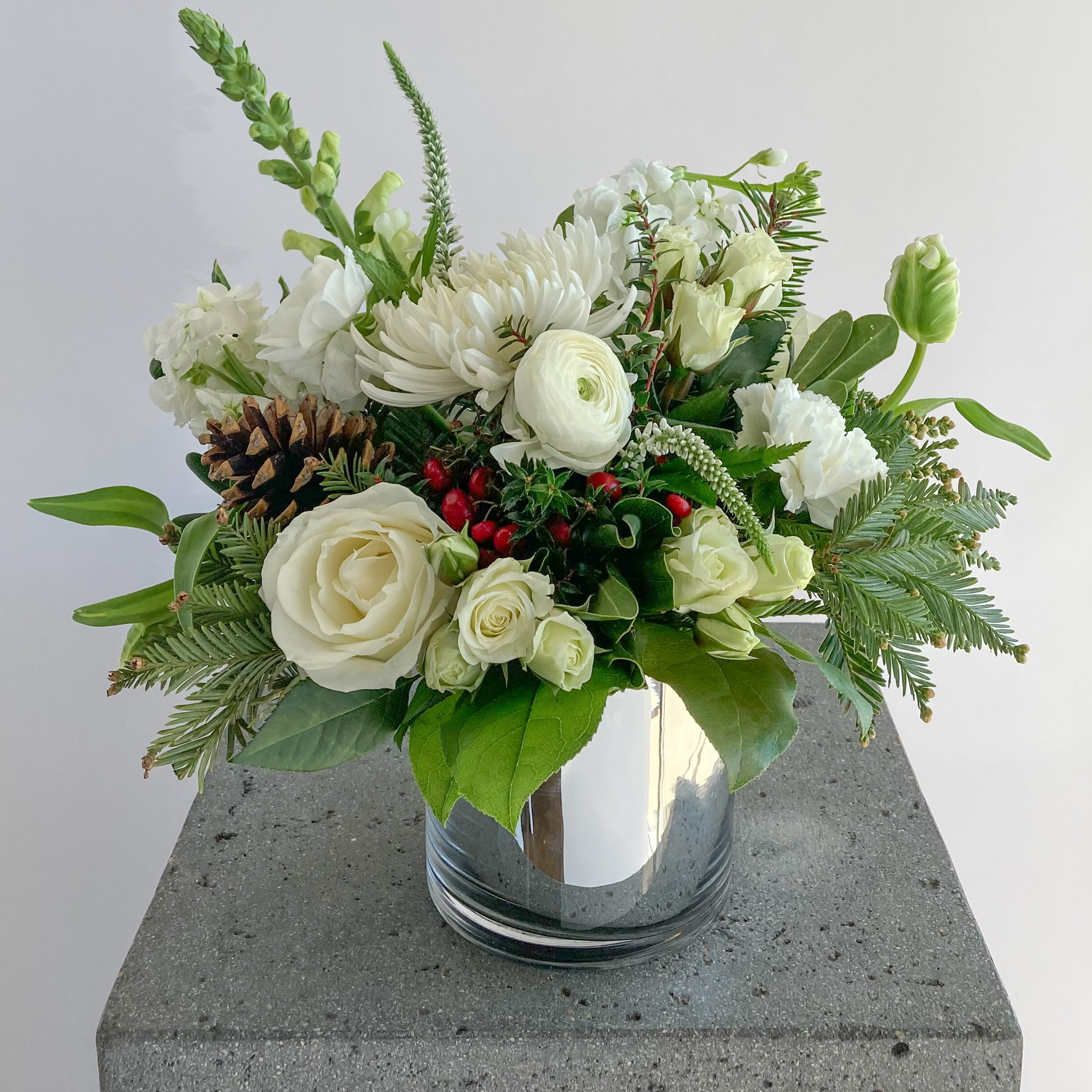 Floral arrangement with white flowers and greenery in a silver vase on a gray pedestal.