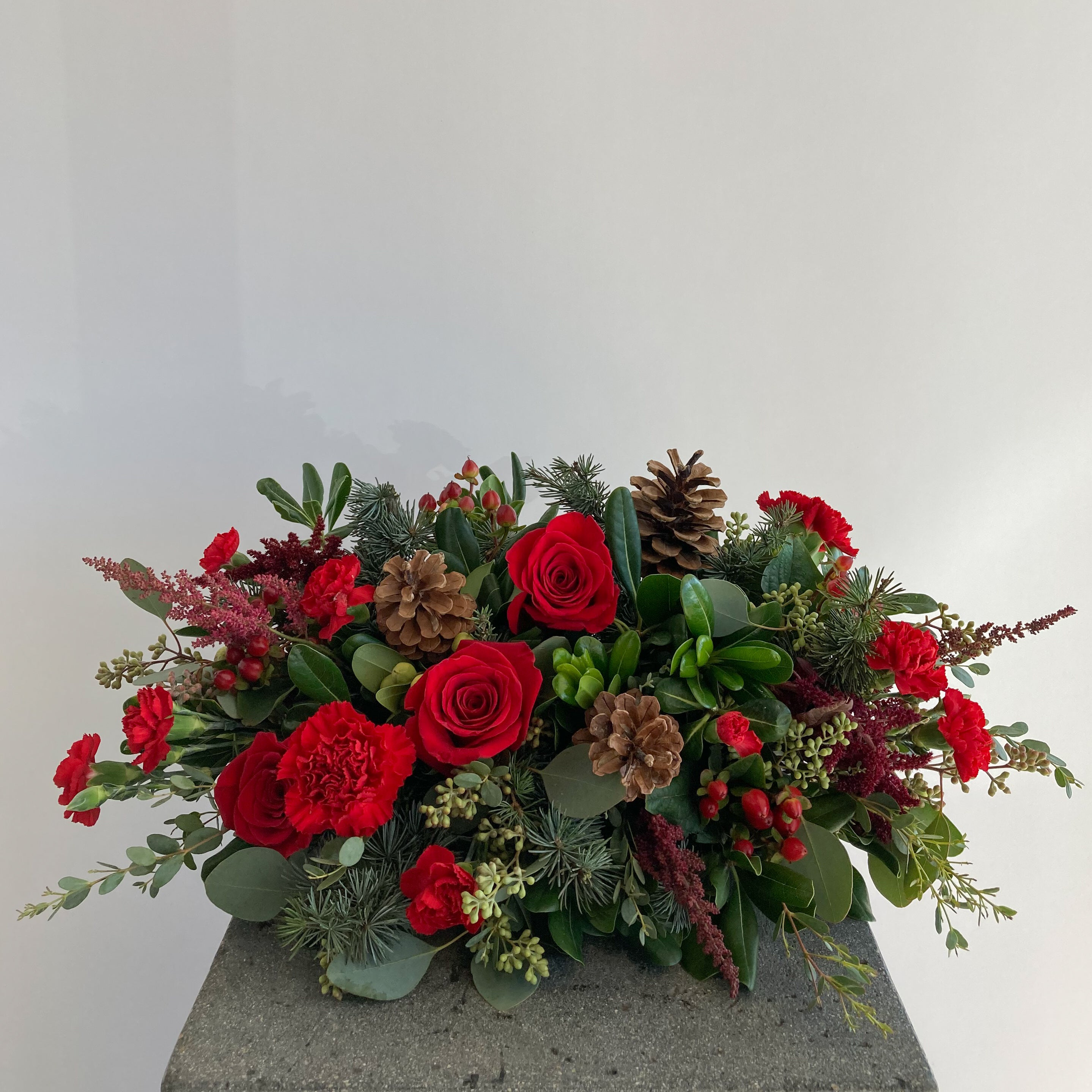 long and low centerpiece arrangement with red flowers, Christmas greens, and pine cones