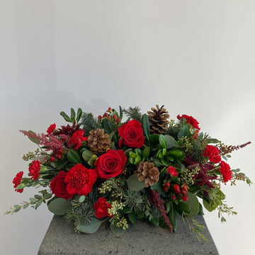 long and low centerpiece arrangement with red flowers, Christmas greens, and pine cones