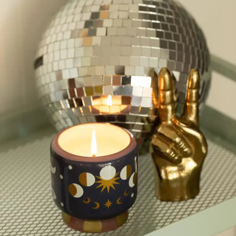 Candle in a decorative holder with a disco ball and gold hand sculpture in the background.