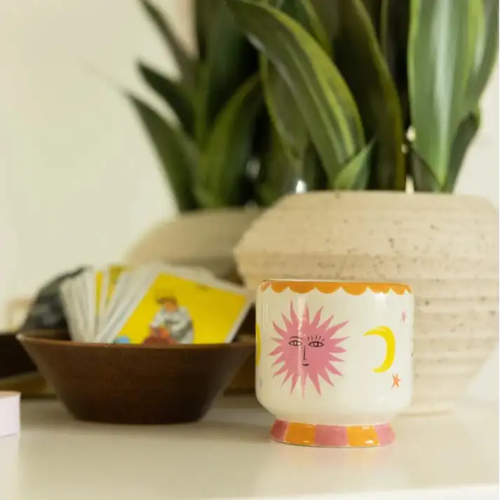 Ceramic mug with sun design on a surface with plants and cards in the background