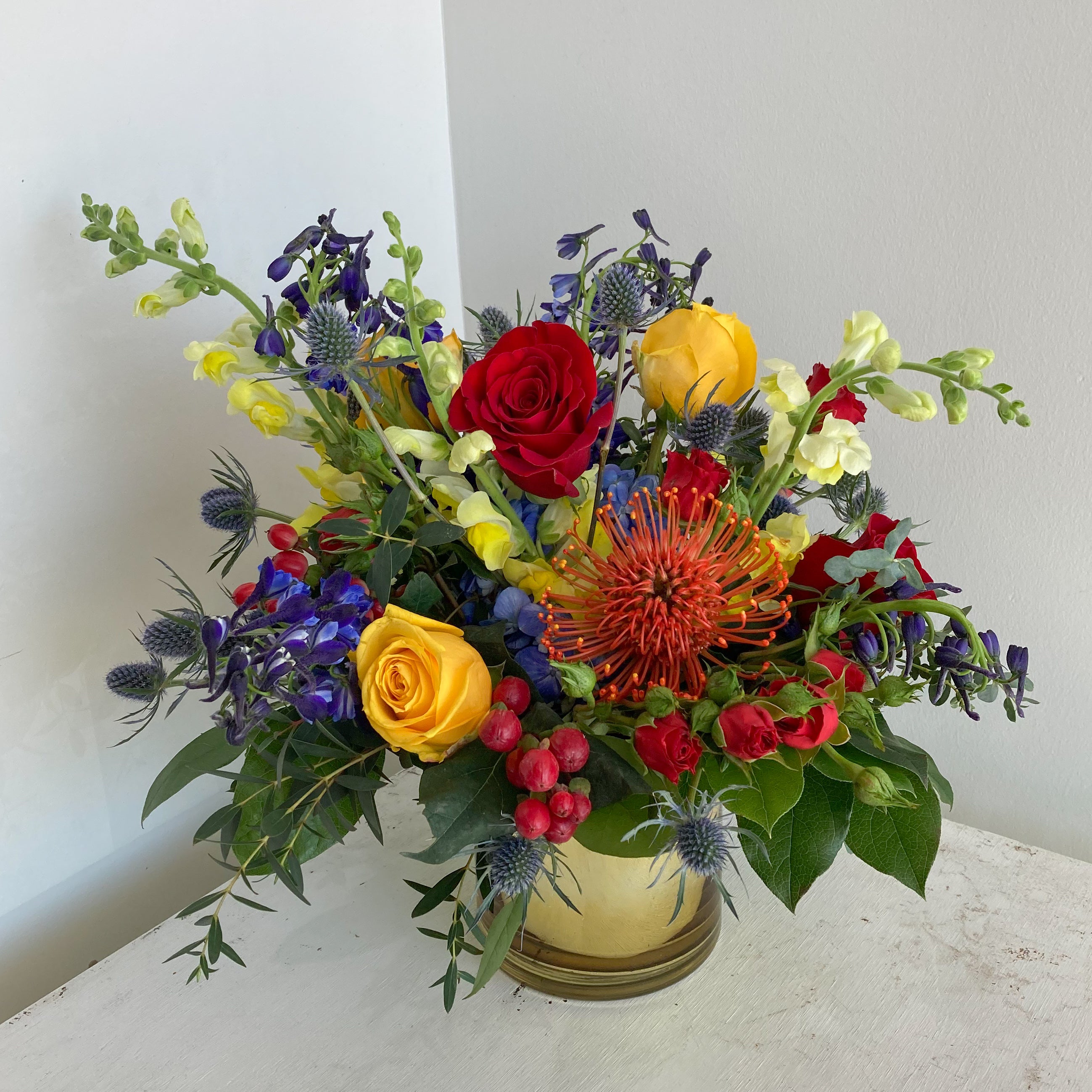 Blue, red, and yellow flower arrangement in a gold vase inspired by a superhero theme supporting The Archer Foundation fundraiser