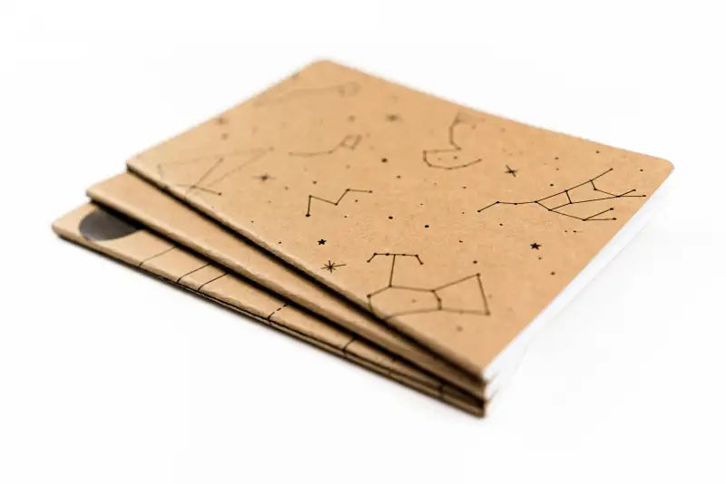 Three brown notebooks with star constellation designs on a white background
