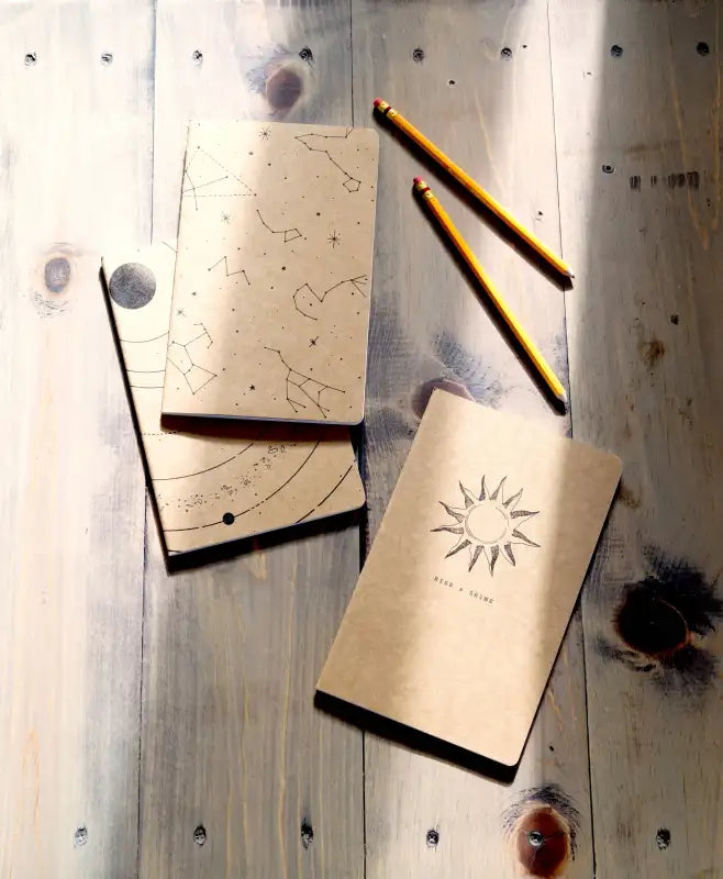 Two notebooks with celestial designs on a wooden surface