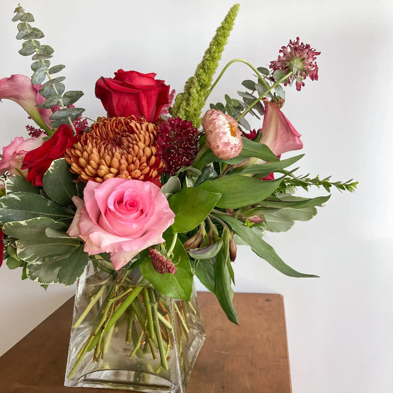 Bouquet of flowers in a clear vase on a wooden surface with a white background