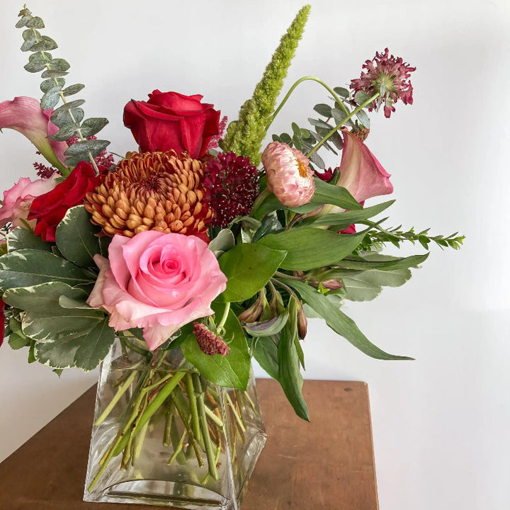 Bouquet of flowers in a clear vase on a wooden surface with a white background