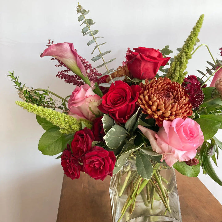 Bouquet of red and pink flowers in a clear vase on a wooden surface with a white background