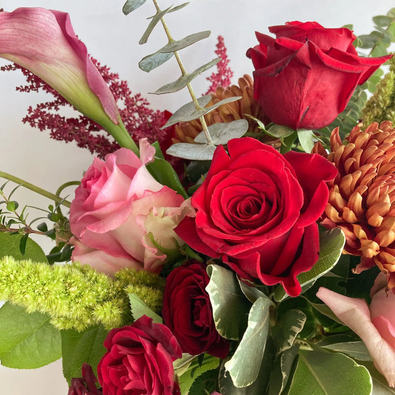 Bouquet of red roses and pink flowers with greenery on a light background