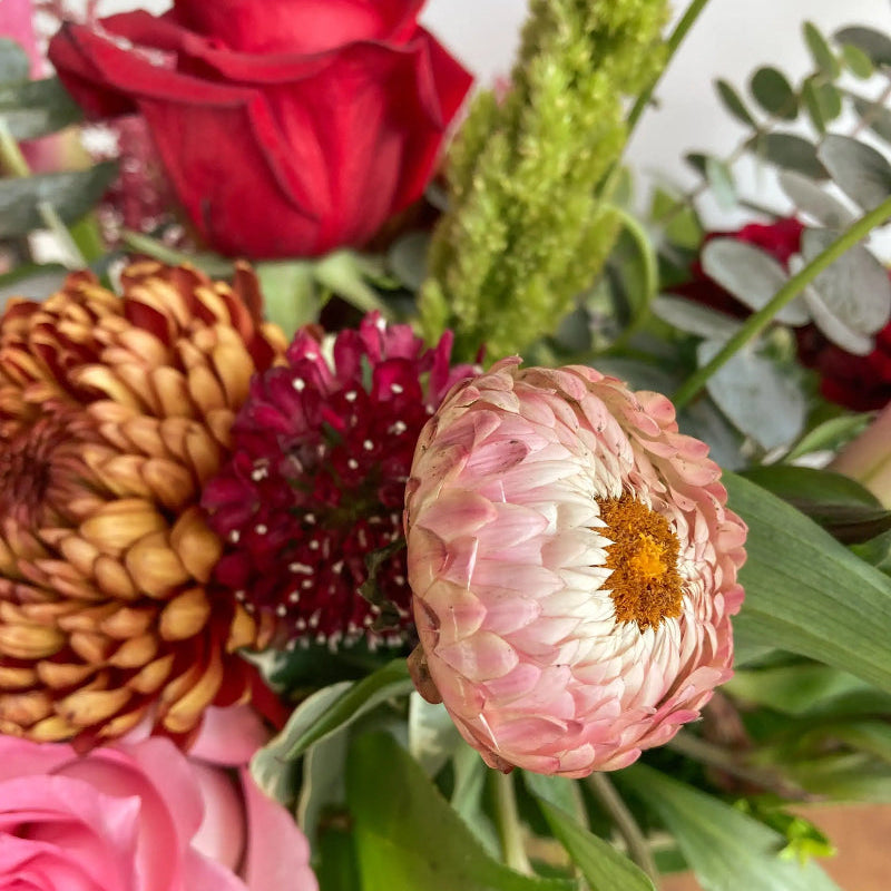 Bouquet of flowers including red roses, pink and yellow dahlias, and greenery.