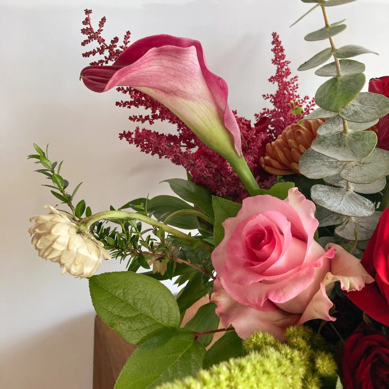 Bouquet of flowers with pink calla lily, roses, and greenery on a white background