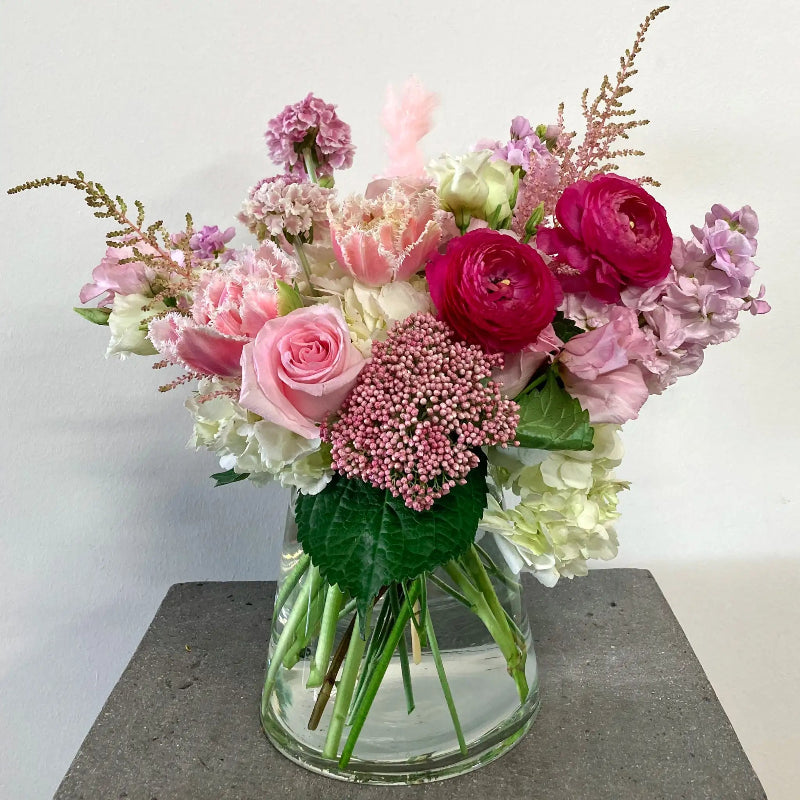Bouquet of pink and green flowers in a clear vase on a gray surface with a white background
