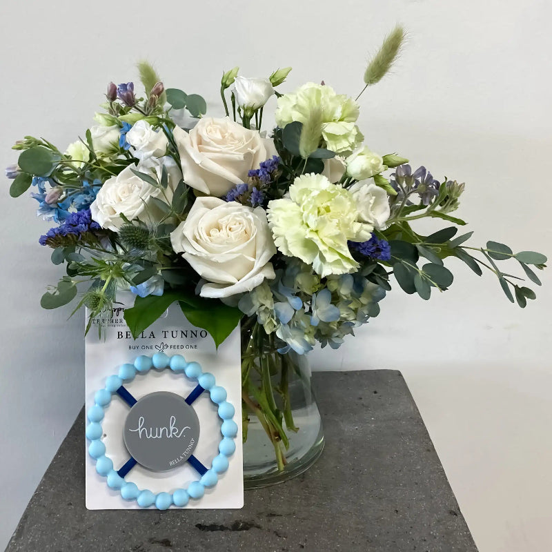 Bouquet of flowers in a glass vase with a Bella Tunno product on a gray surface.