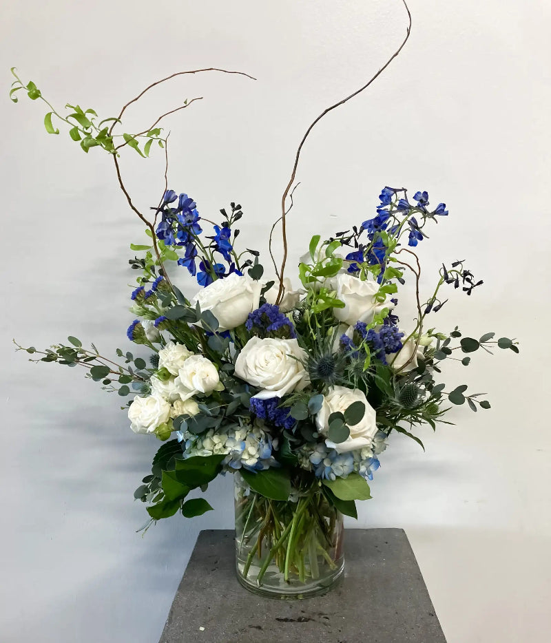 Floral arrangement with blue and white flowers in a clear vase on a gray surface.