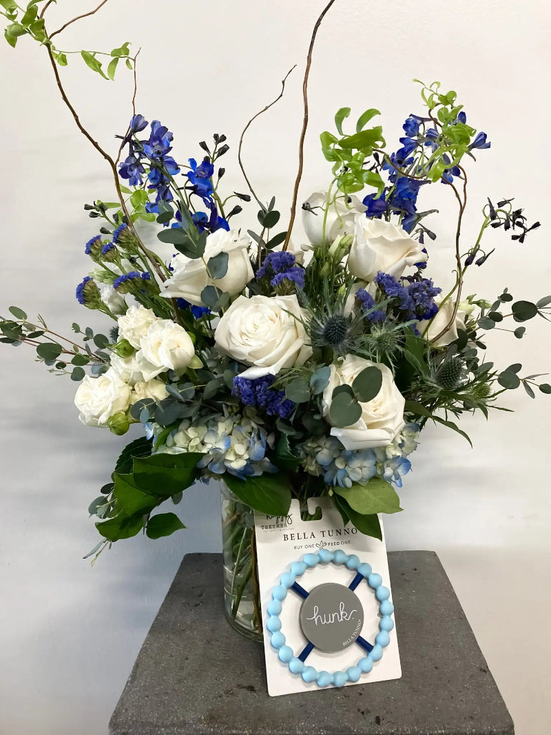 Floral arrangement with white and blue flowers in a clear vase on a gray surface.