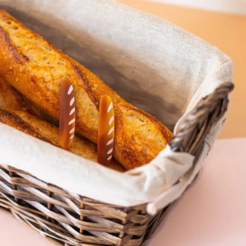 Loaf bread in a wicker basket with baguette hair clips on a neutral background