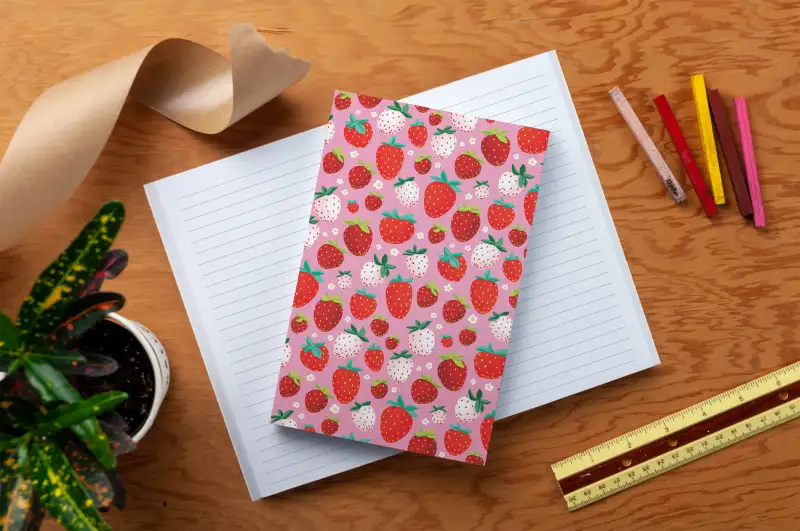 Notebook with strawberry pattern on a wooden surface with stationery items