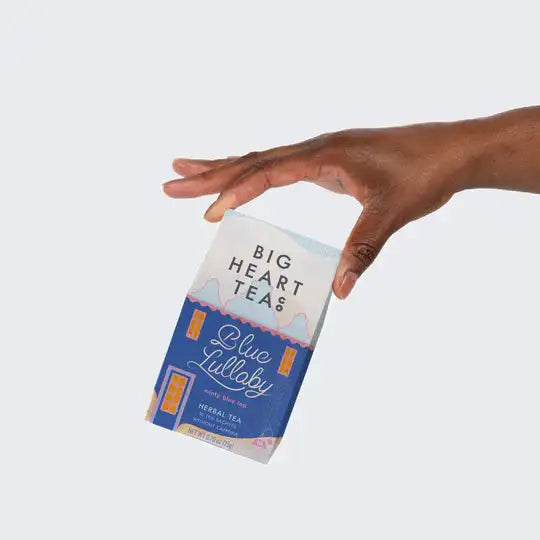 Hand reaching for a box of Big Heart Teas Blue Lullaby tea on a light gray background