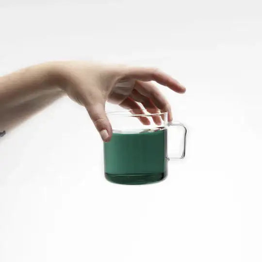 Hand holding a glass mug with green liquid on a white background