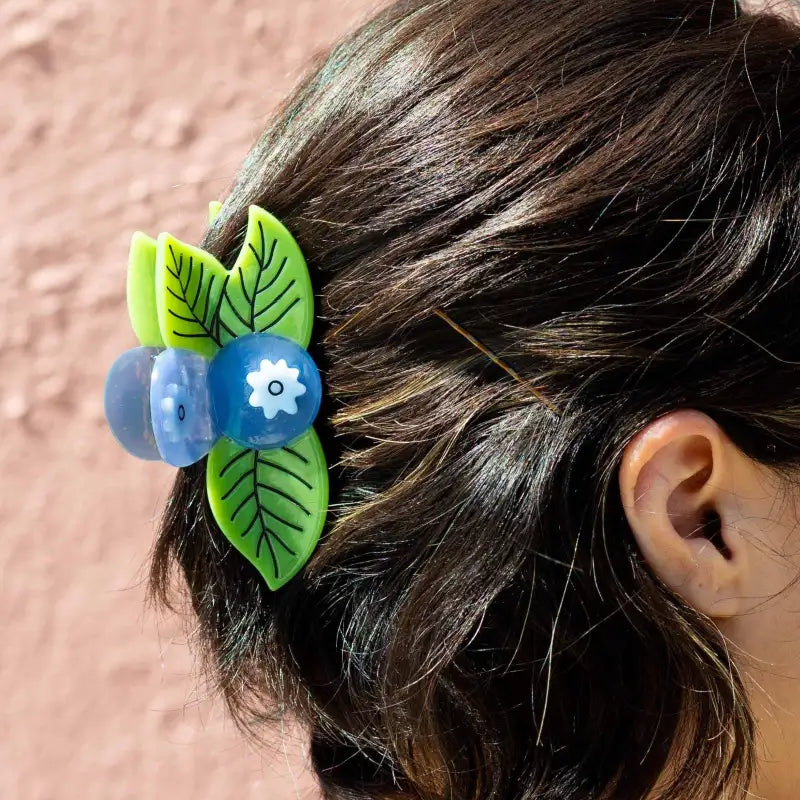 Hair clip with green leaves and blue flowers on a person's head against a pink background