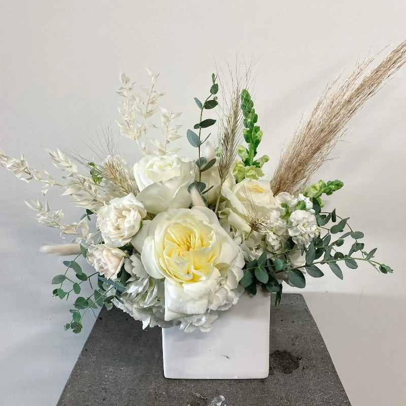 Floral arrangement with white and yellow flowers in a white vase on a gray surface.