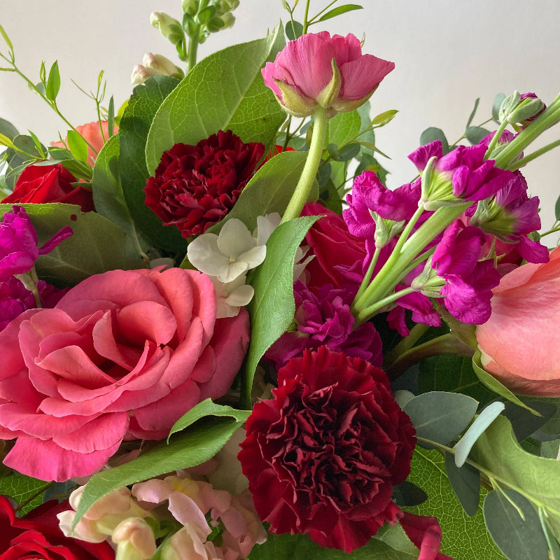 Bouquet of red and pink flowers with green leaves on a light background