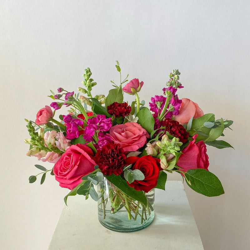 Bouquet of colorful flowers in a clear vase on a light surface with a light background