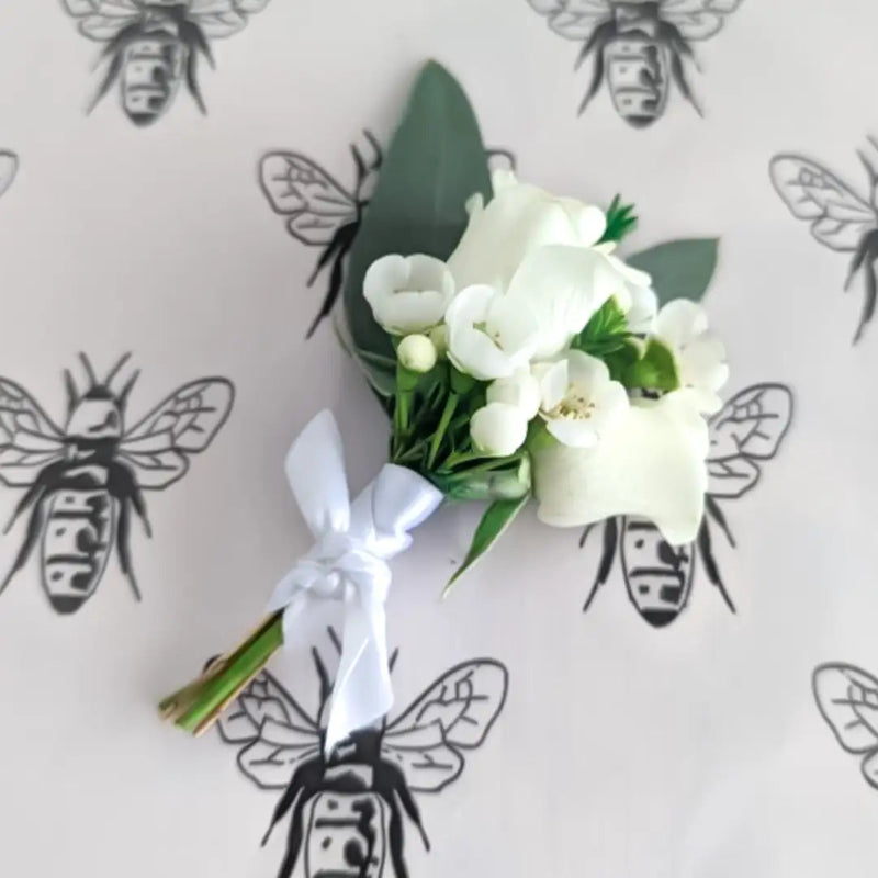White floral corsage with green leaves on a light gray background with bee illustrations.