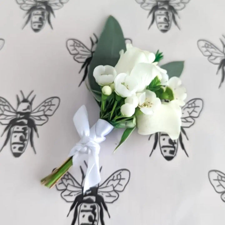 White floral corsage with green leaves on a light gray background with bee illustrations.