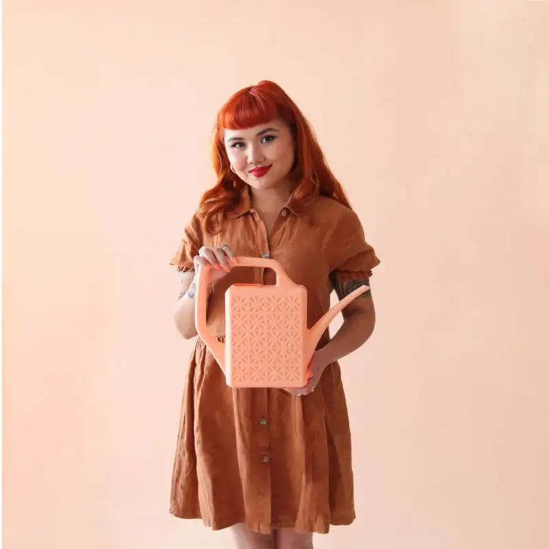 Woman holding a pink watering can against a beige background