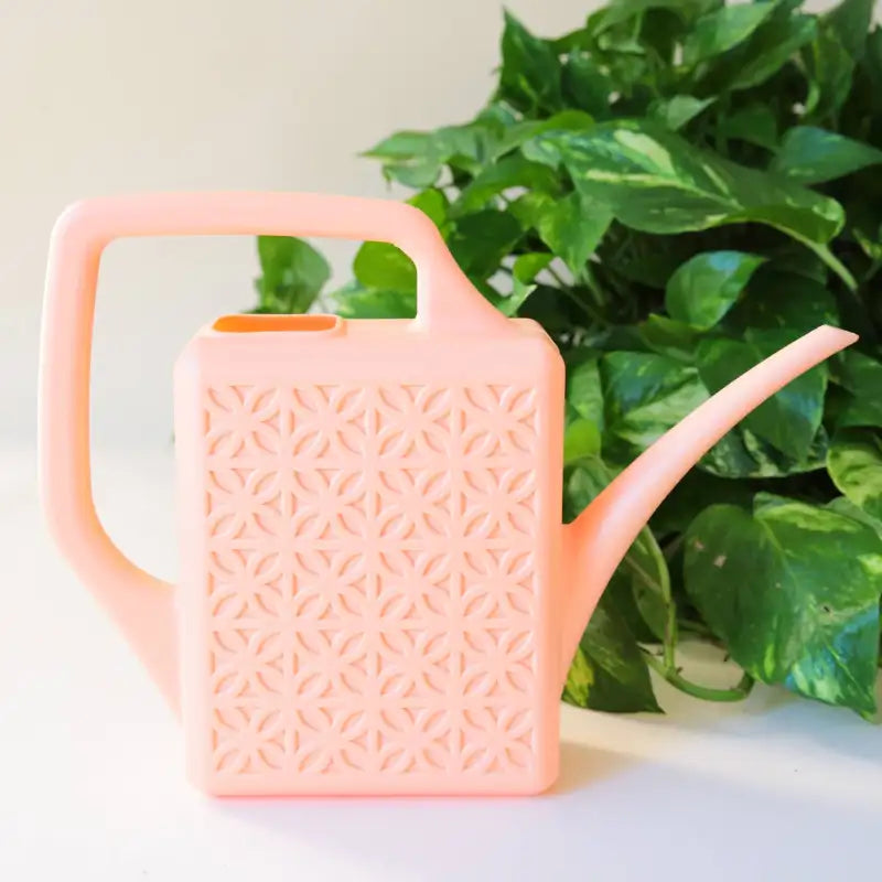 Pink watering can with textured design in front of green leaves