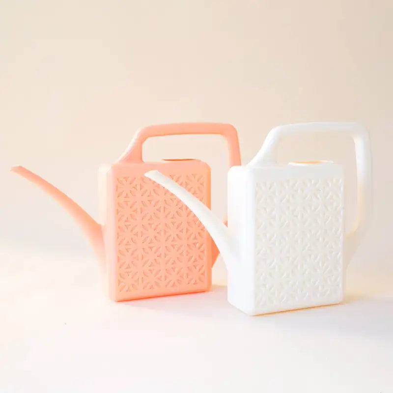Two watering cans, one pink and one white, on a light beige background.