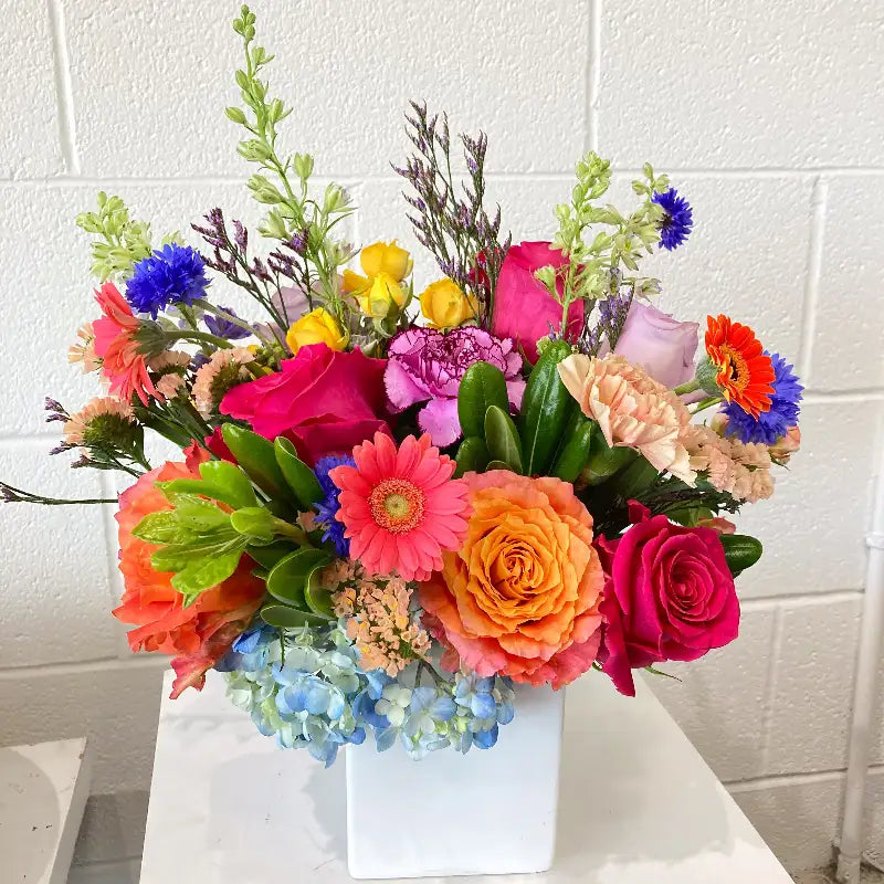 Colorful flower bouquet in a white vase against a white tiled wall.