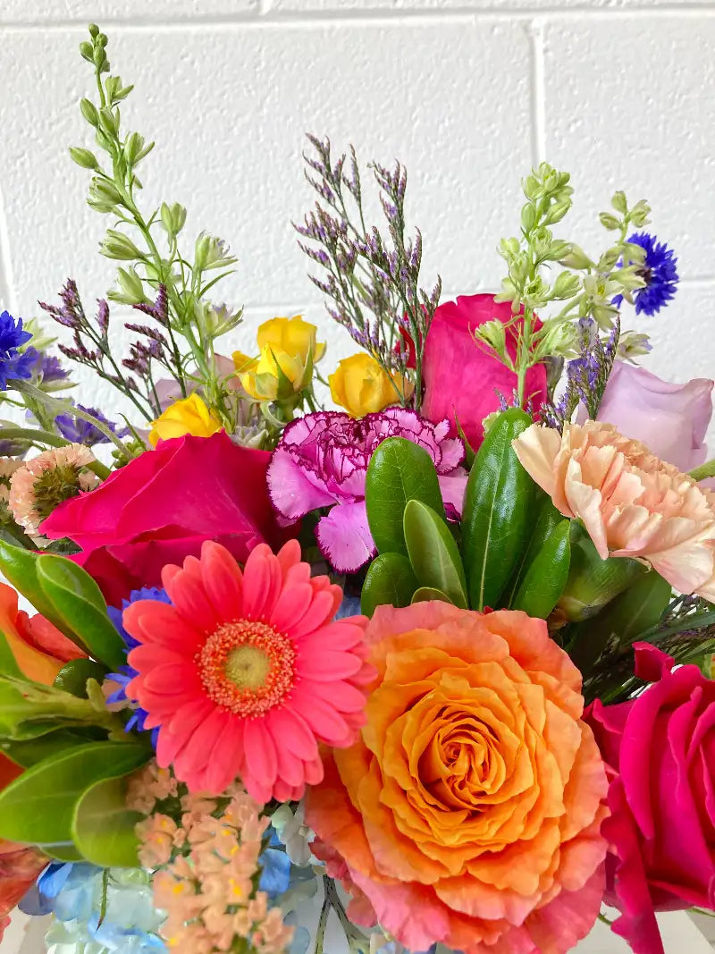 Bouquet of colorful flowers including roses and gerberas against a white brick wall.