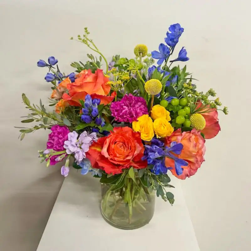 Colorful bouquet of flowers in a clear vase on a white surface with a light gray background