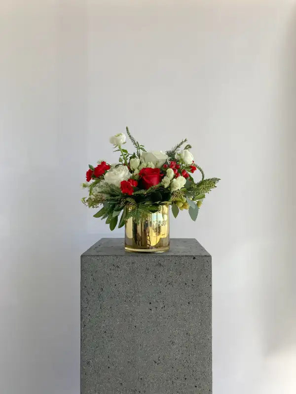 Floral arrangement in a gold vase on a concrete pedestal against a plain background
