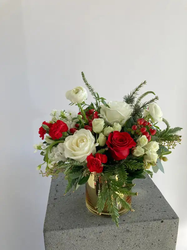 Floral arrangement with red and white flowers on a gray pedestal against a white background