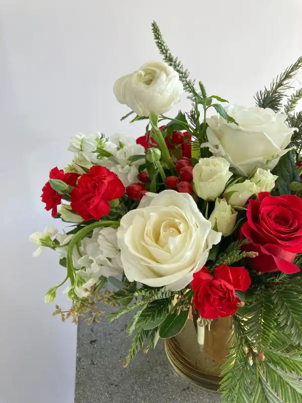 Bouquet of red and white roses with greenery in a gold vase on a light gray background