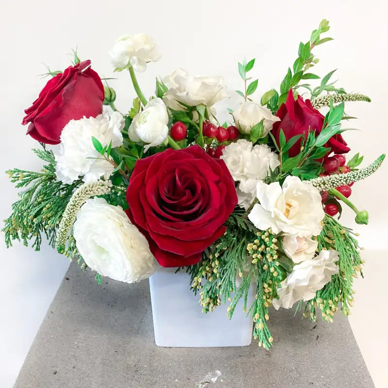 Bouquet of red and white flowers with greenery in a white box on a light background