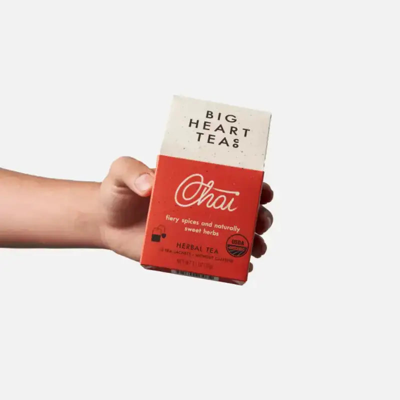 Hand holding a box of Big Heart Teas Chai tea on a white background