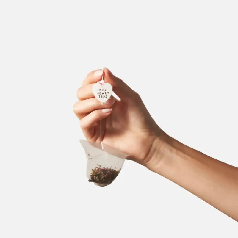 Hand holding a tea bag with loose tea leaves against a white background