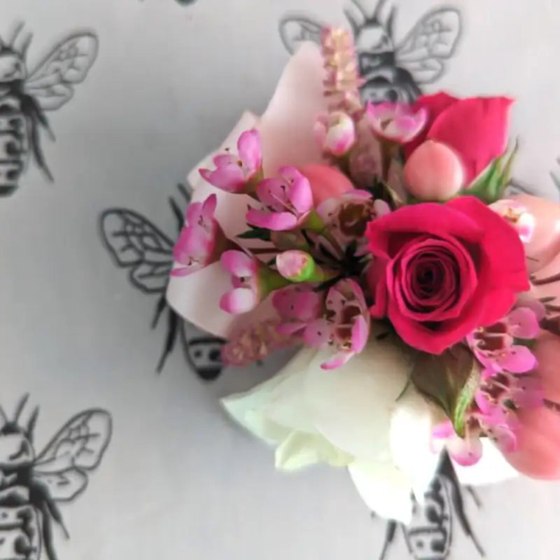 Floral arrangement with pink and red flowers on a white background with black bee illustrations.