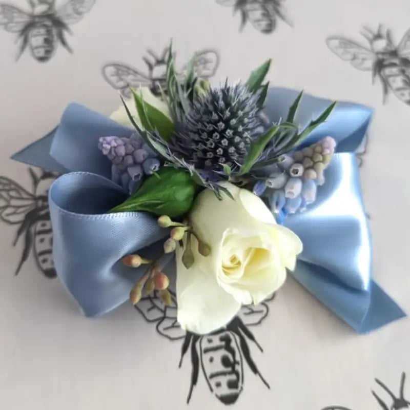 Floral corsage with blue ribbon, white rose, and thistle on a light background