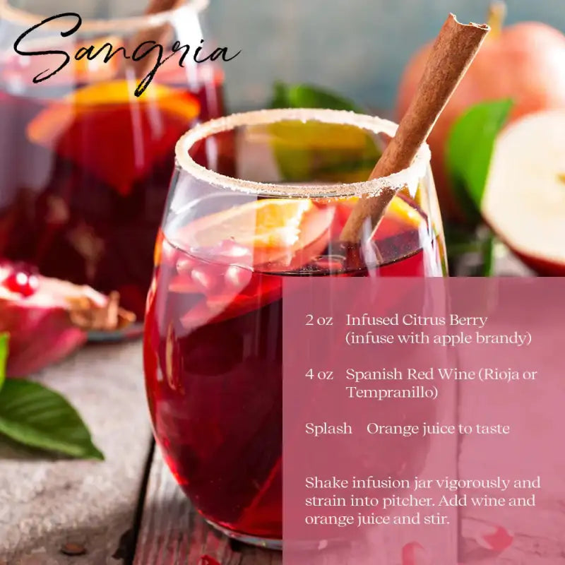 Glass of red sangria with a cinnamon stick, surrounded by fruits on a wooden surface.