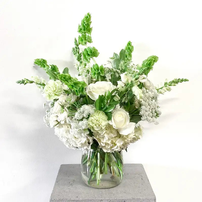 Bouquet of white and green flowers in a clear vase on a light background
