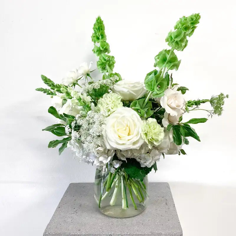 Bouquet of white and green flowers in a clear vase on a light background