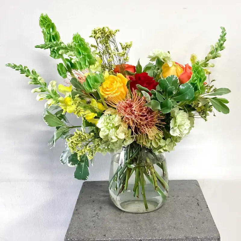Bouquet of flowers in a clear vase on a gray pedestal with a white background