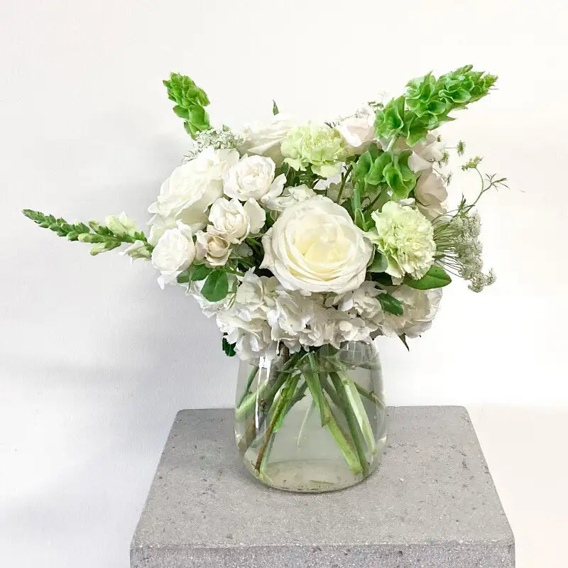 Bouquet of white and green flowers in a clear vase on a gray pedestal with a white background